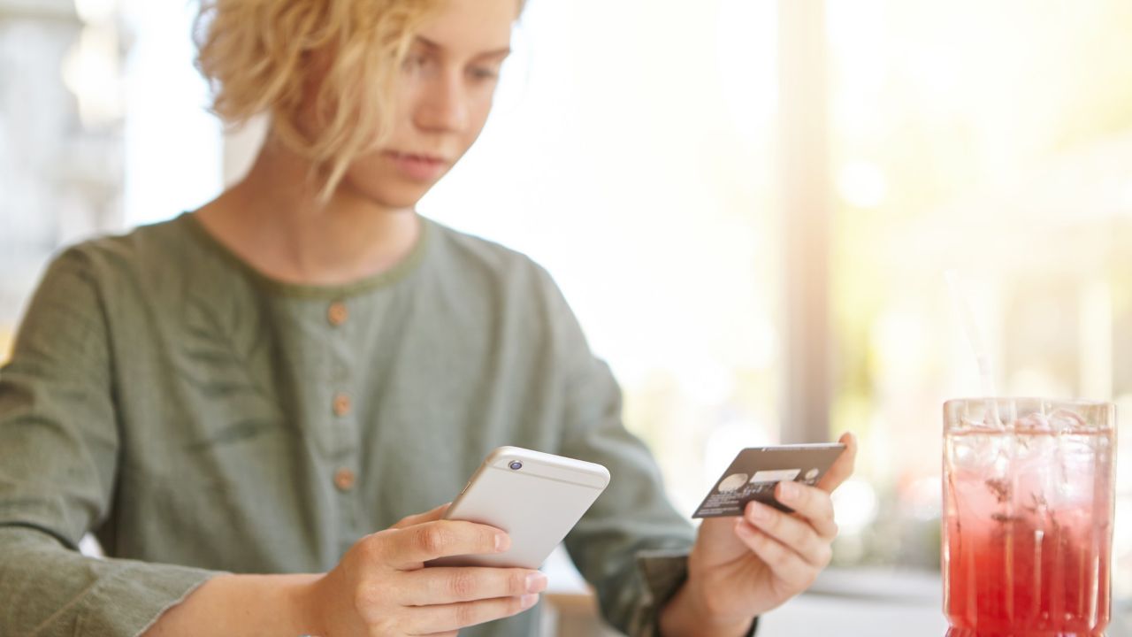 donna bionda che tiene il telefono e la carta di credito
