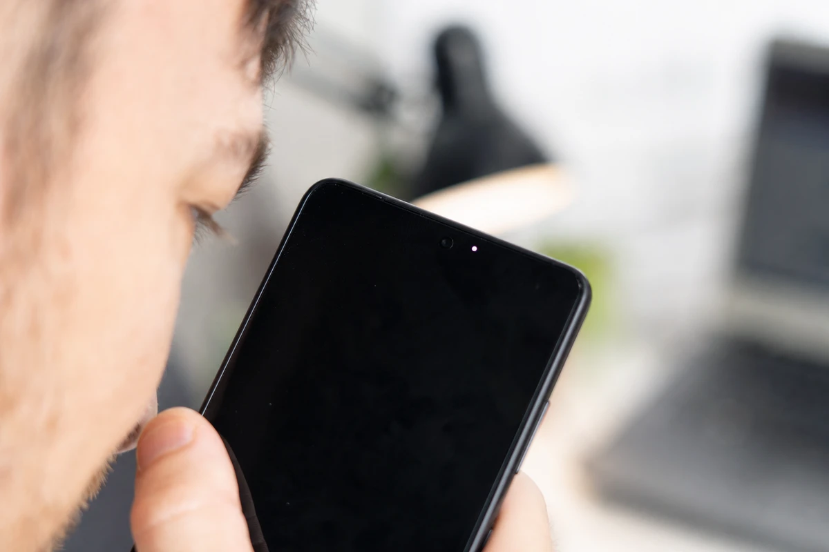 Smartphone vicino all’orecchio con schermo scuro e piccolo puntino luminoso in alto