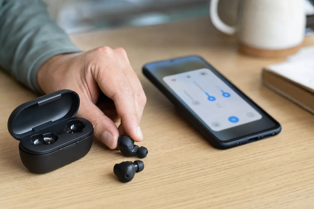 Auricolari Bluetooth con custodia aperta accanto a uno smartphone Android con cursori del volume sullo schermo