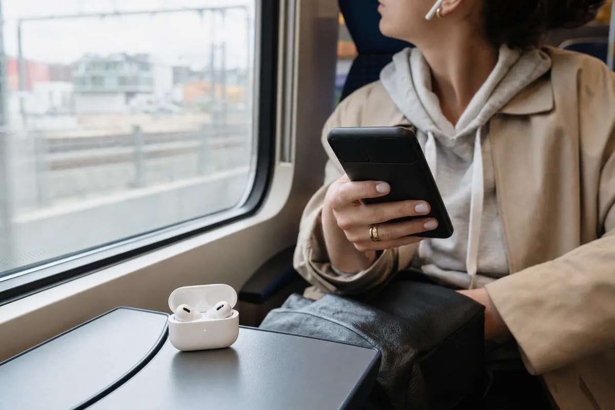 Passeggera in treno con smartphone in mano e custodia aperta di auricolari wireless sul tavolino