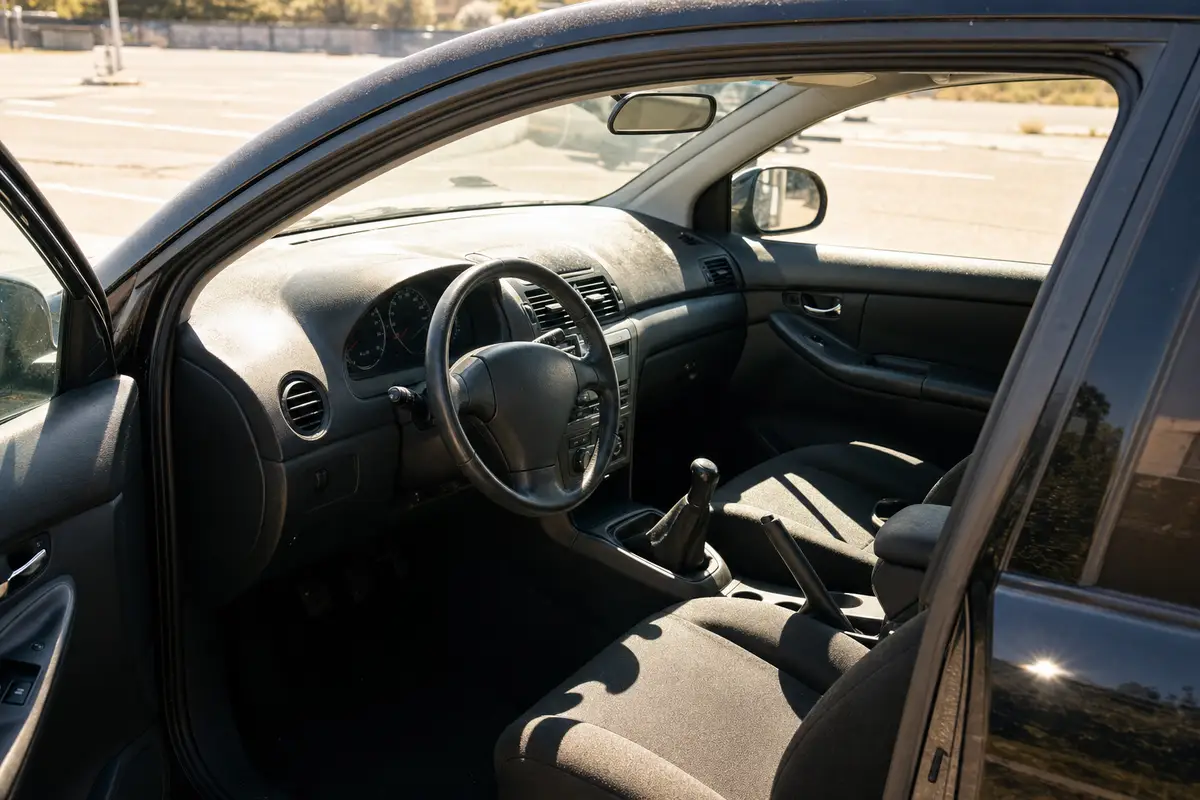 Interni di un’auto scura parcheggiata al sole, visti dalla portiera aperta, con cruscotto e sedili illuminati
