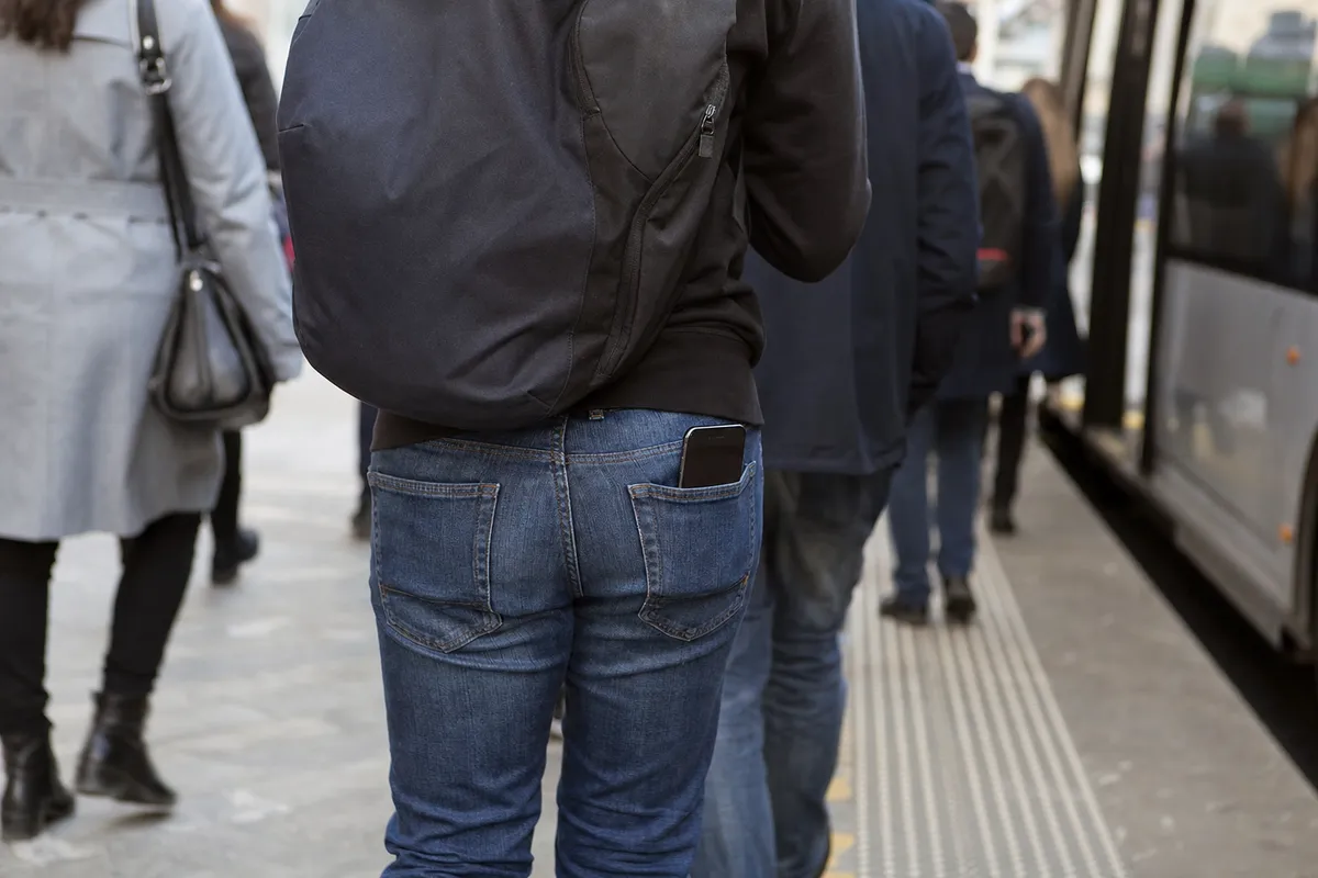 Smartphone che sporge dalla tasca posteriore dei jeans di un pendolare in mezzo alla folla alla fermata