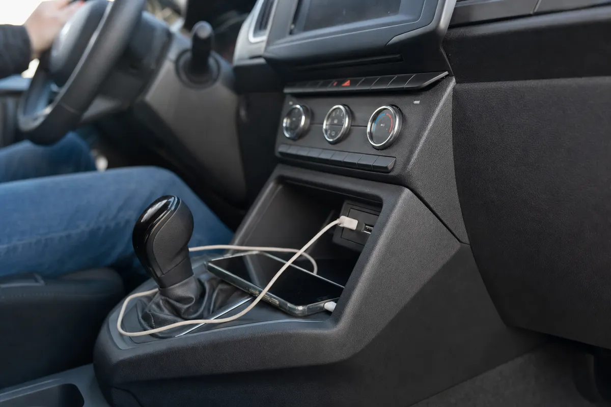 Smartphone collegato alla porta USB dell’auto con cavo sul tunnel centrale, vicino alla leva del cambio