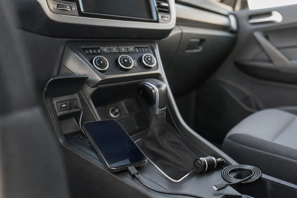 Smartphone collegato alla porta USB dell’auto sulla console centrale, con caricatore 12V e cavo USB-C accanto