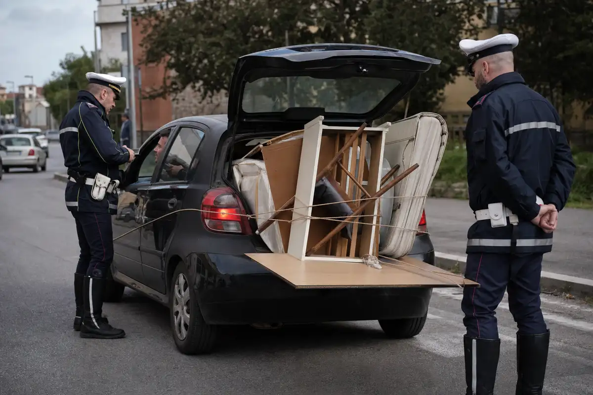 Auto fermata con portellone aperto e mobili sporgenti legati con corde, controllata da due agenti