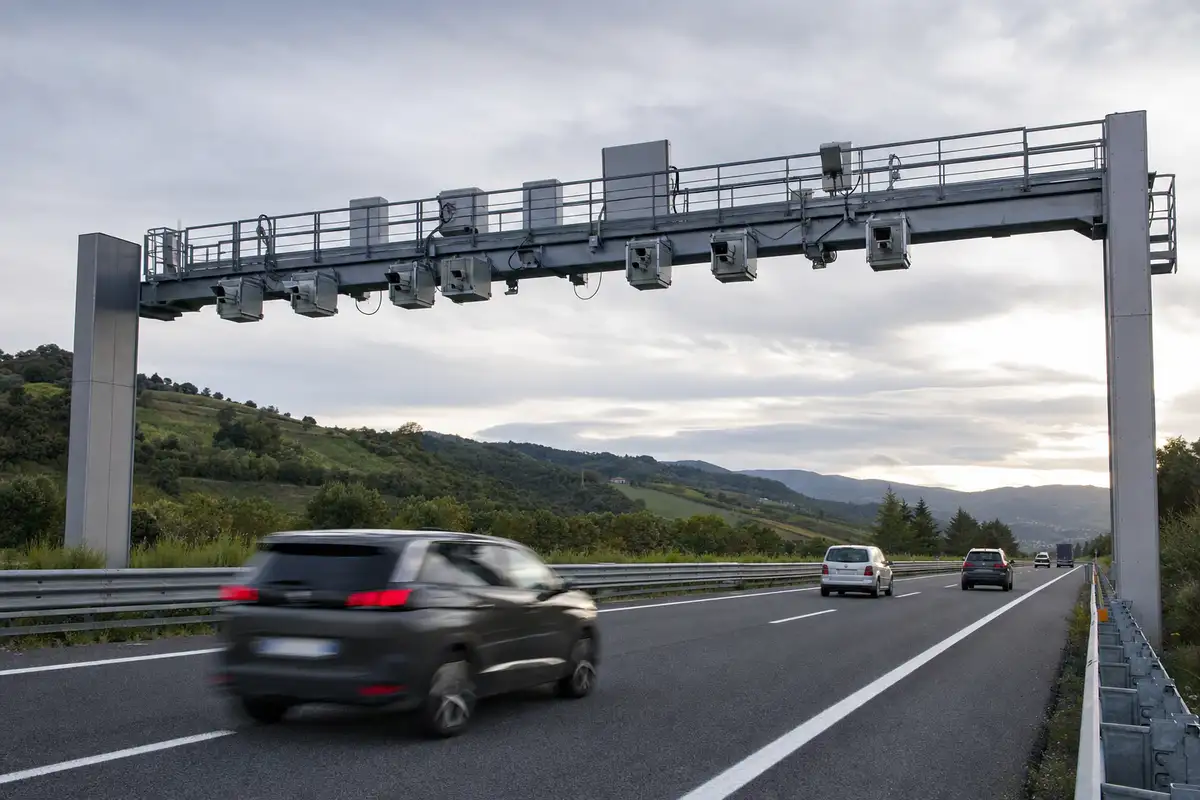 Portale con telecamere sopra un’autostrada, auto in transito senza casello tra colline verdi