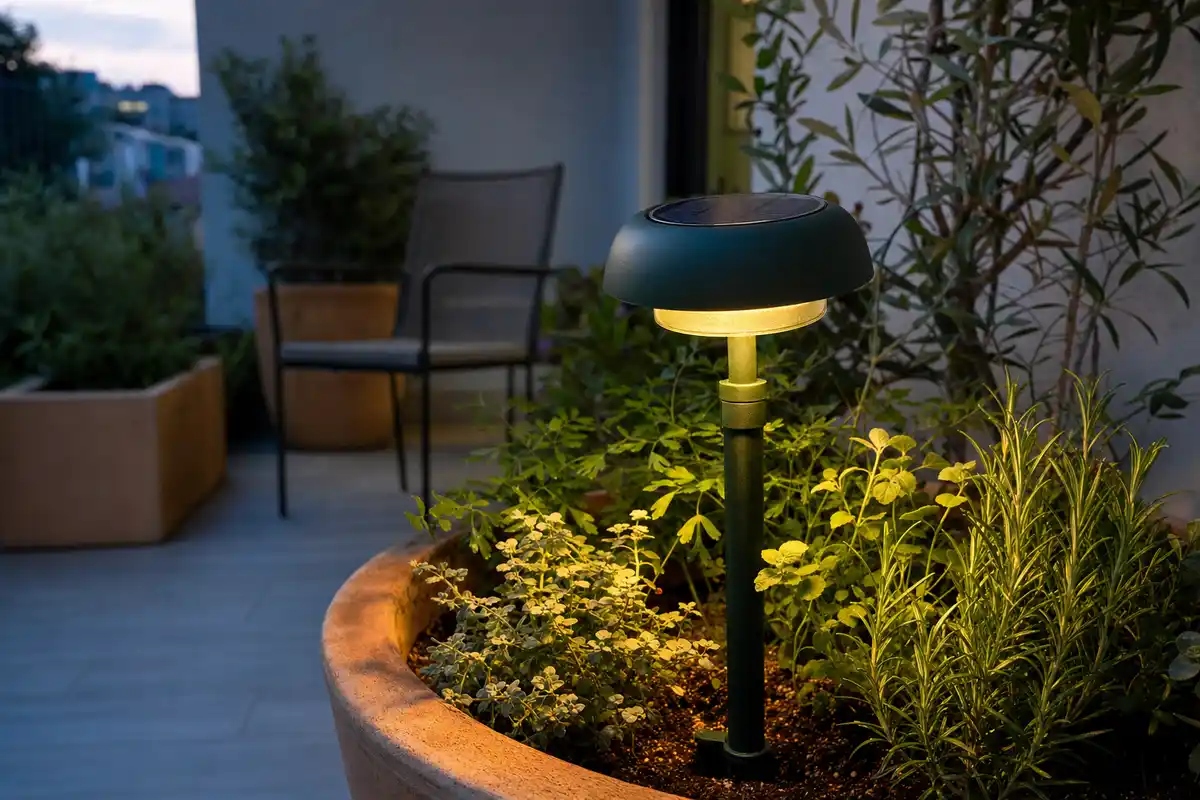 Lanterna solare da esterno verde scuro accesa in un grande vaso in terracotta su una terrazza al tramonto
