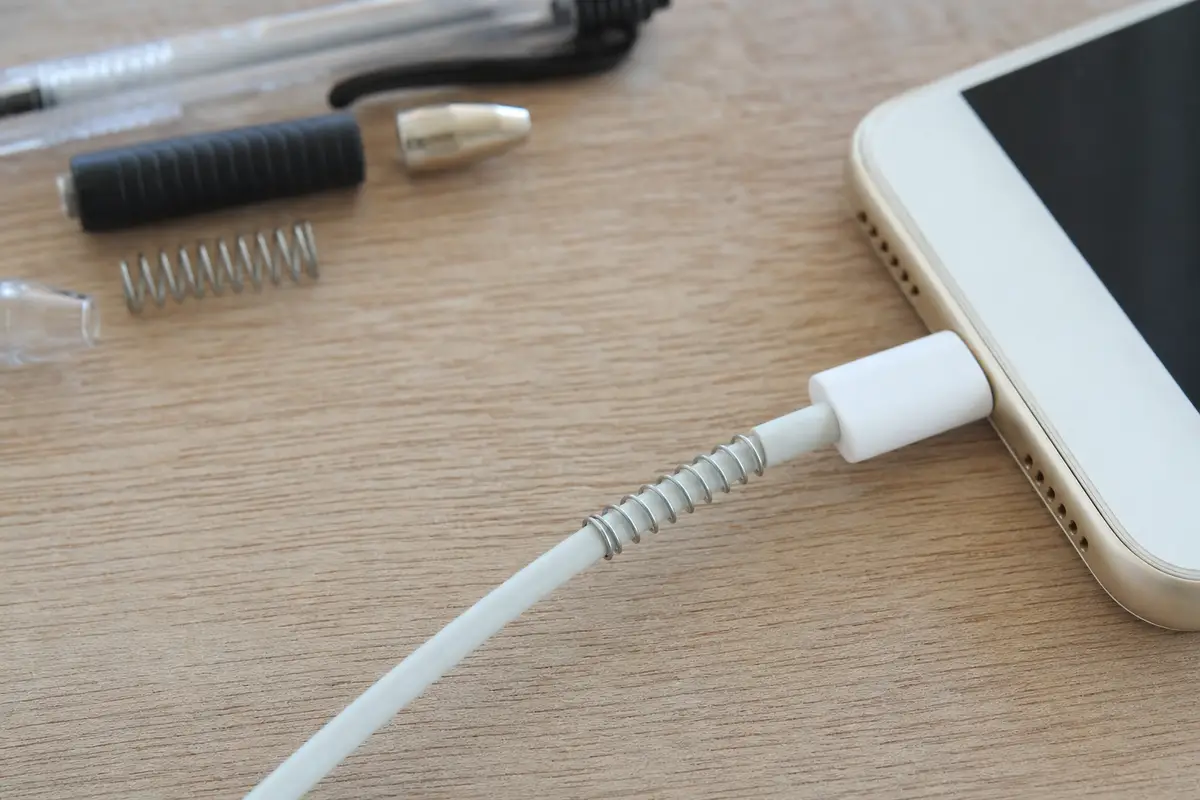 Cavo di ricarica bianco collegato allo smartphone con una molla metallica avvolta vicino al connettore