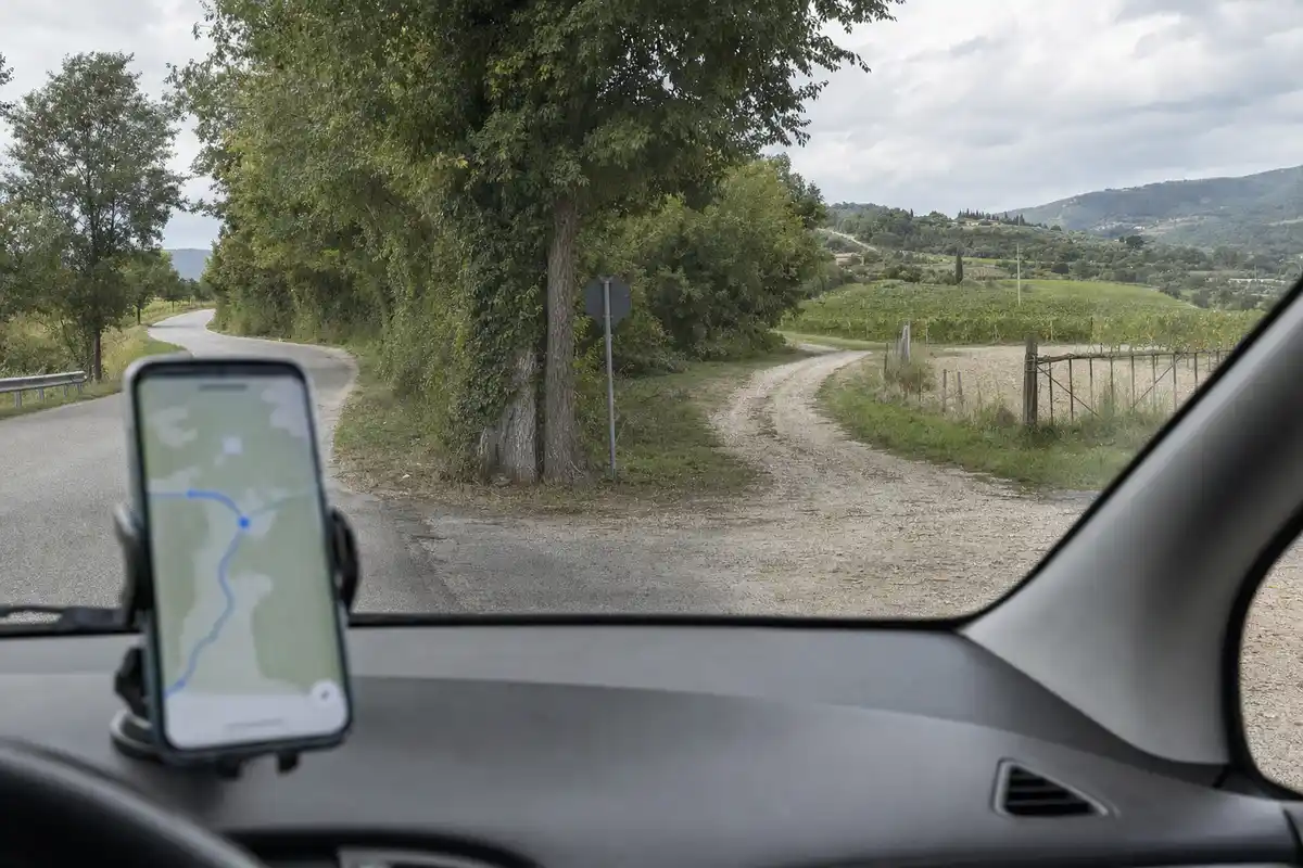 Smartphone con mappa sul cruscotto davanti a un bivio tra strada asfaltata e sterrata in campagna