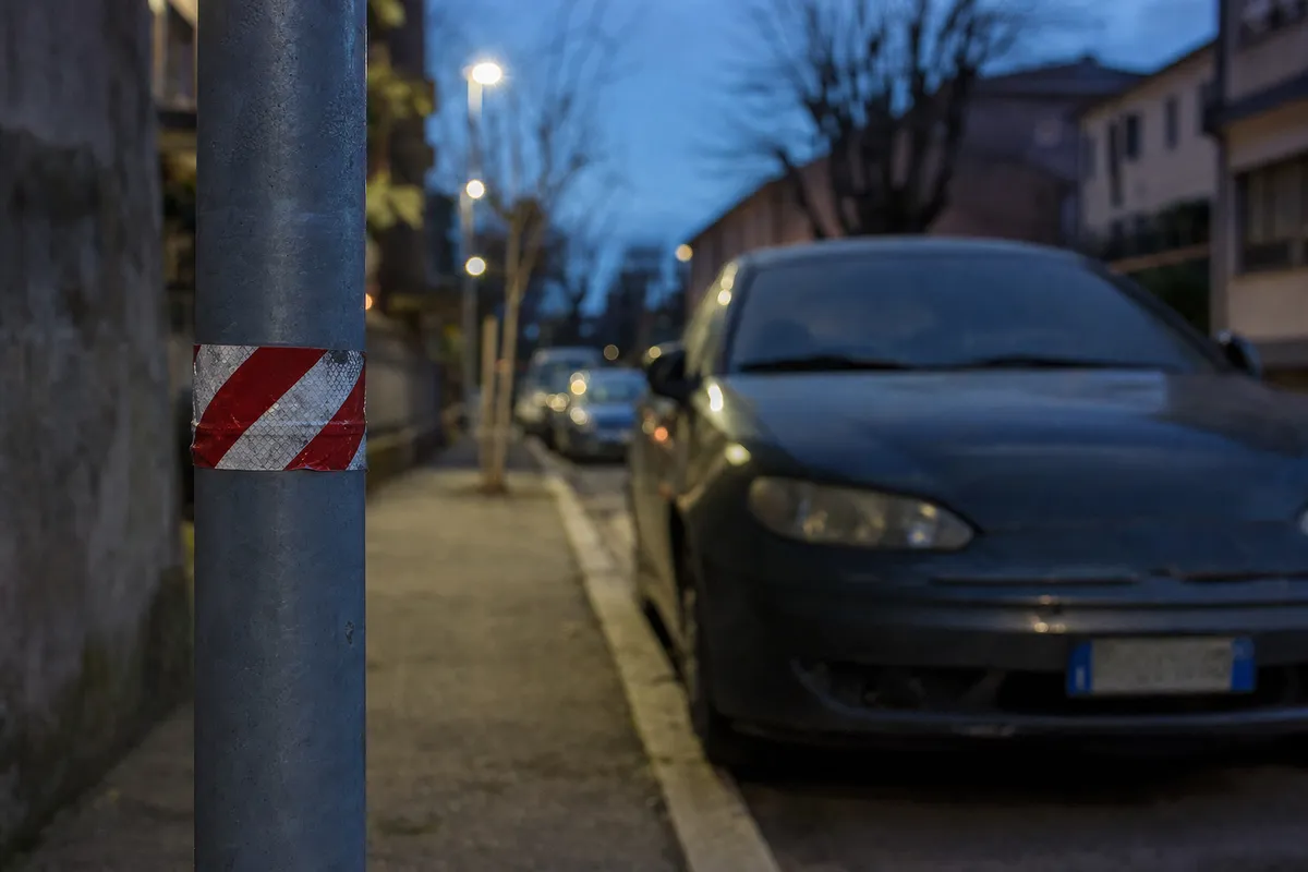 Nastro riflettente rosso e bianco avvolto su un palo della luce, con auto parcheggiata sullo sfondo al crepuscolo