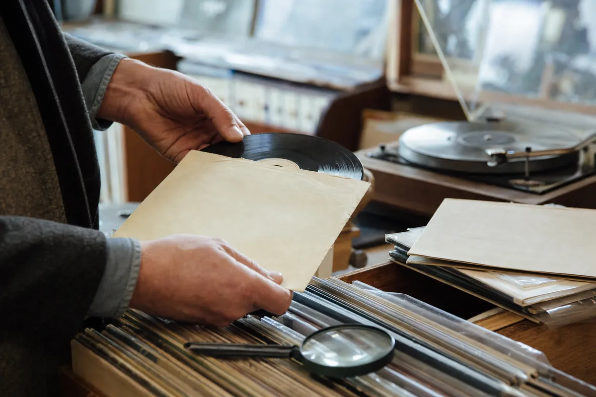 Mani che estraggono un disco in vinile 45 giri da una busta di carta, con giradischi sullo sfondo