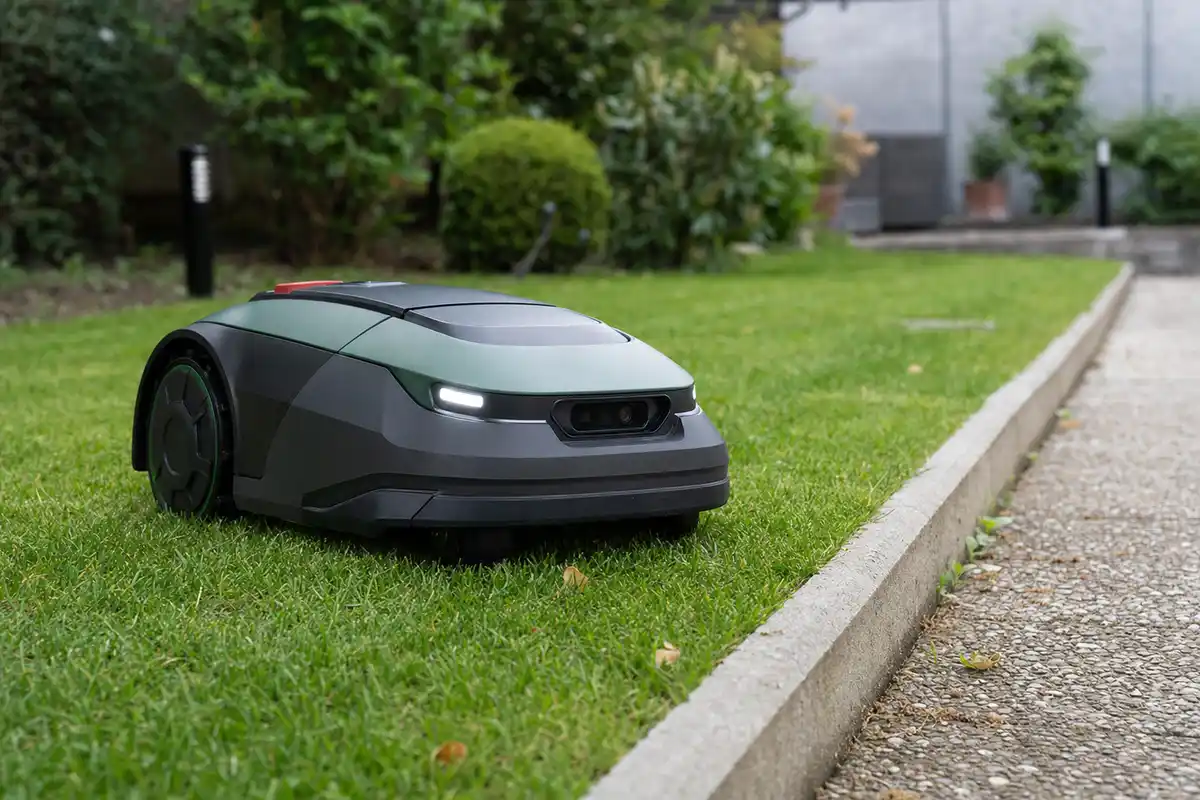 Robot tagliaerba su prato vicino a un cordolo in cemento, con fari LED e sensore frontale