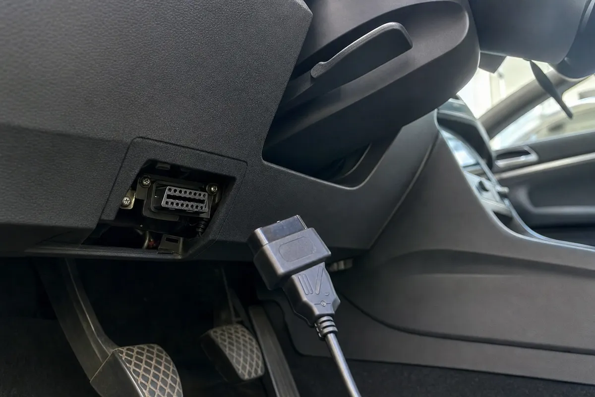 Porta OBD II sotto il cruscotto con connettore di alimentazione vicino, nell’abitacolo di un’auto