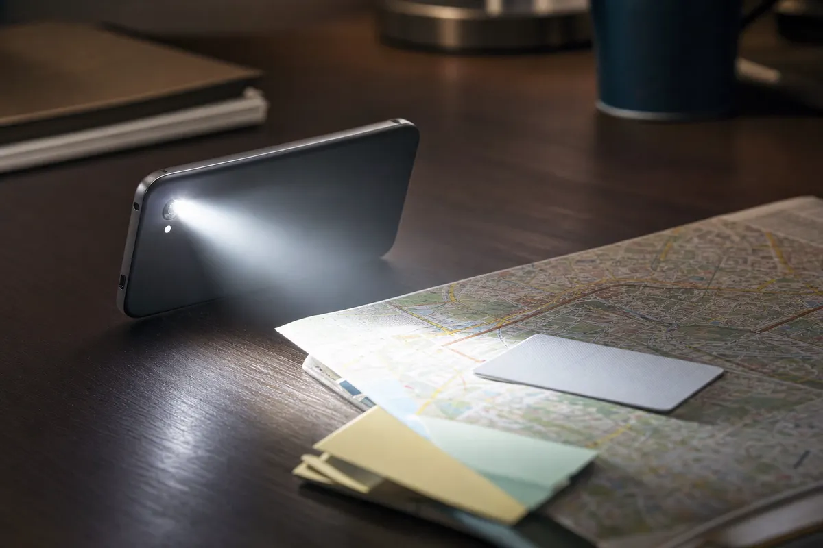 Smartphone con torcia accesa su scrivania, fascio di luce su mappa cittadina, card capovolta e foglietti