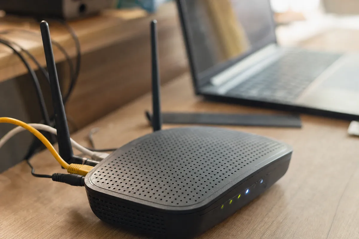Router Wi‑Fi su scrivania con cavi Ethernet e LED accesi, laptop sfocato sullo sfondo