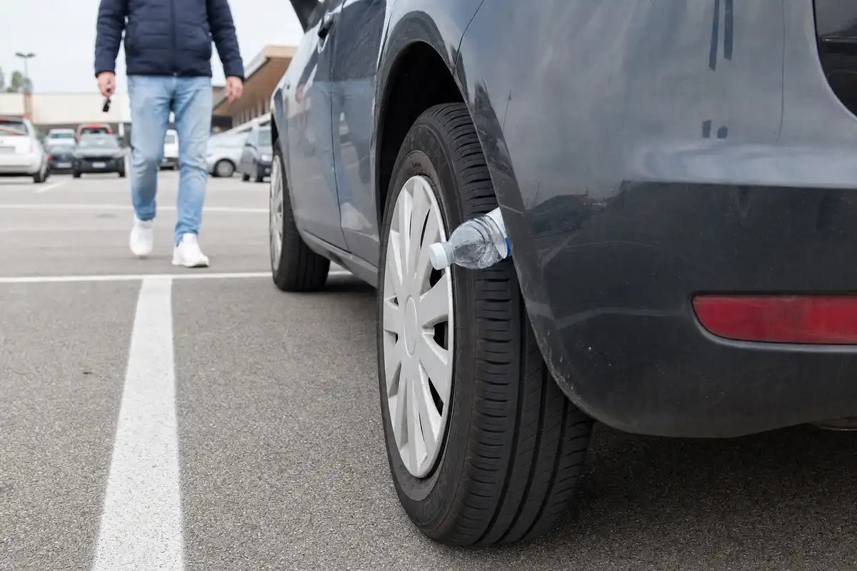 Bottiglietta di plastica incastrata nella ruota posteriore di un’auto in un parcheggio, con una persona che si avvicina