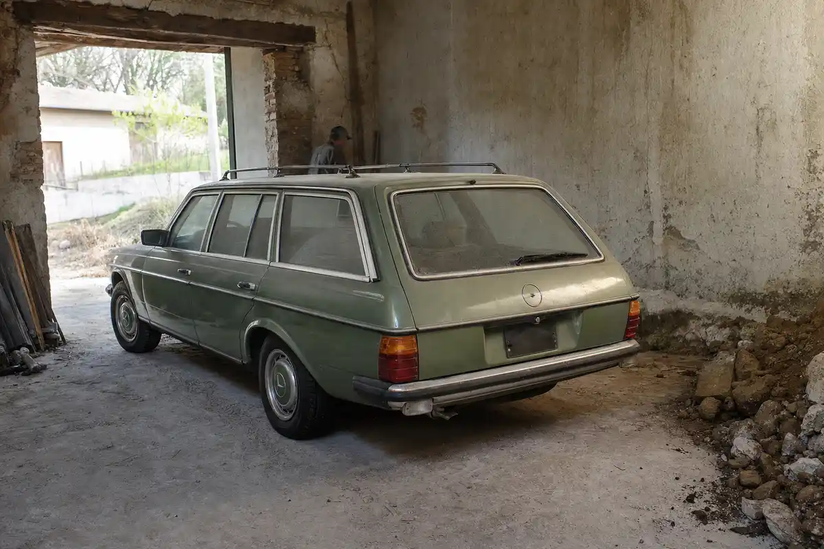 Station wagon verde anni Settanta impolverata in un garage abbandonato, vista posteriore a tre quarti