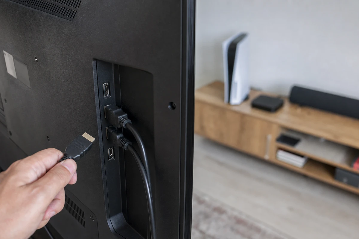 Retro di una smart TV con due cavi HDMI inseriti e una mano che tiene un terzo connettore vicino alle porte