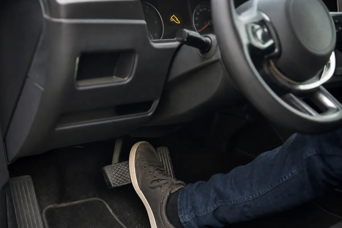 Piede con scarpa che preme il pedale del freno, con spia a forma di scarpa accesa sul cruscotto
