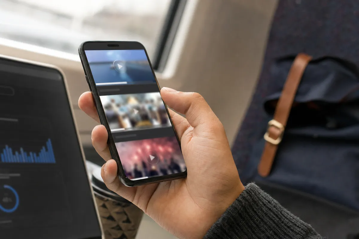 Mano che tiene uno smartphone con feed di video e anteprime con barra di caricamento, accanto a un grafico di consumo dati