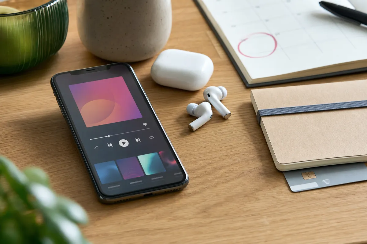 Smartphone con app di musica, auricolari wireless, taccuino con carta di pagamento e calendario con data cerchiata