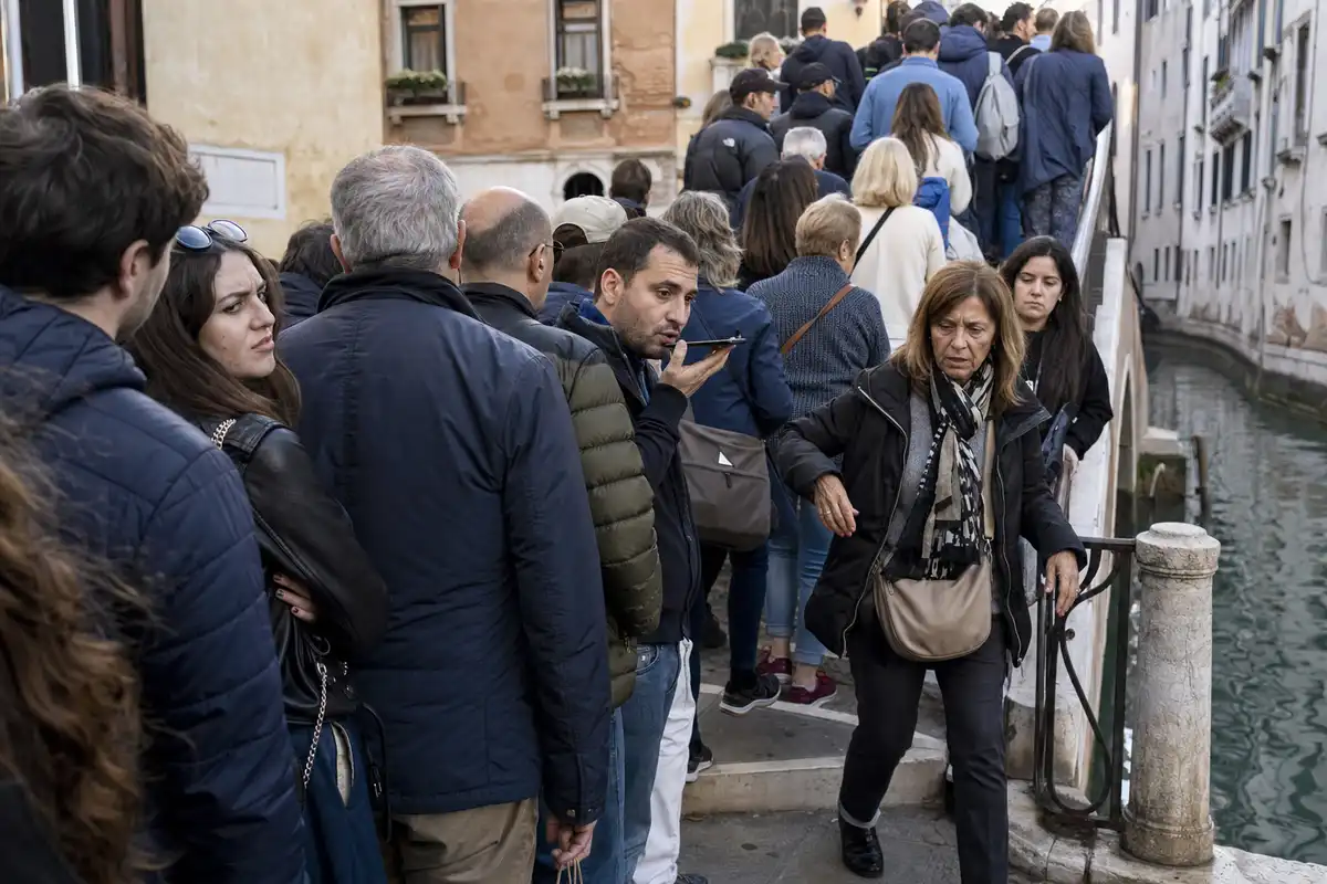 Folla in coda su un ponte stretto a Venezia, con una persona che parla al telefono a voce alta e passaggio affollato